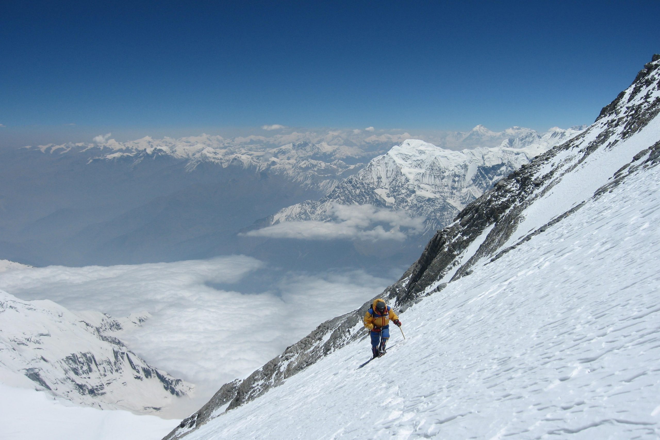 Alpinista ascendiendo montaña muy nevada con nubes