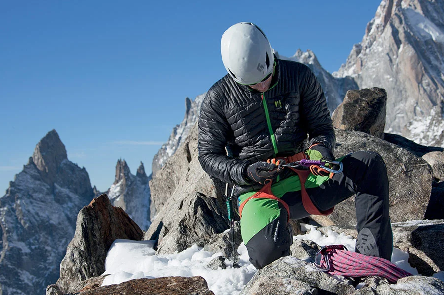 Alpinista comprobando un mosquetón con chaquetas de alpinismo