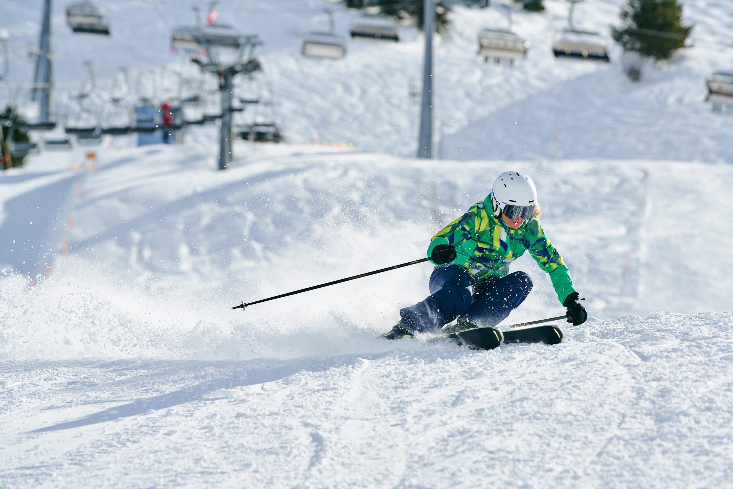Mujer esquiando en pistas con casco blanco y chaqueta verde