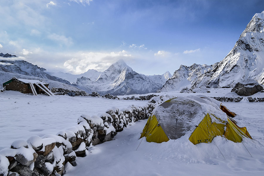 Tienda de campaña amarilla con nieve entre montañas nevadas