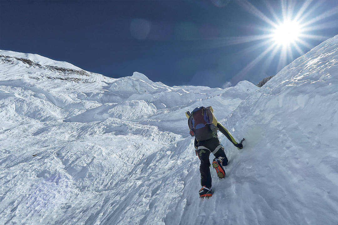 Alpinista ascendiendo montaña nevada con piolet y crampones